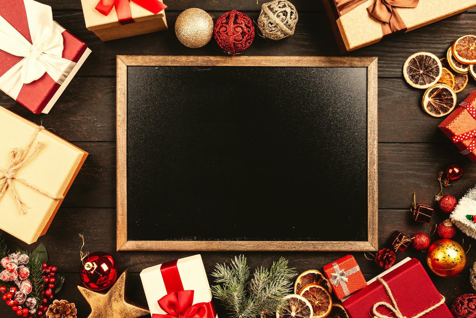 Top-down view of a blackboard surrounded by Christmas gifts and decorations with space for text.
